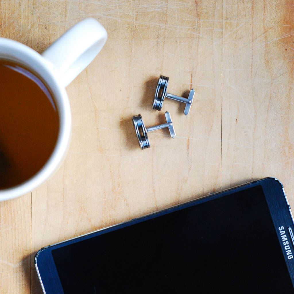 Paguro Upcycle recycled bicycle chain cufflinks displayed next to a cup of coffee and a Samsung smartphone