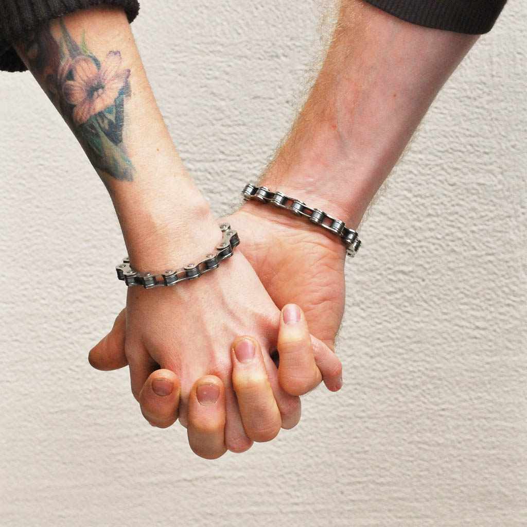 Two hands wearing matching recycled bike chain bracelet from Paguro Upcycle holding each other