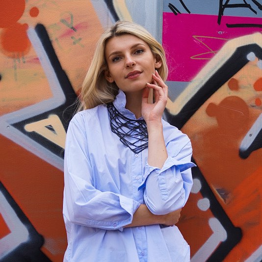 Woman wearing a black upcycled rubber necklace from Paguro Upcycle with colorful graffiti background