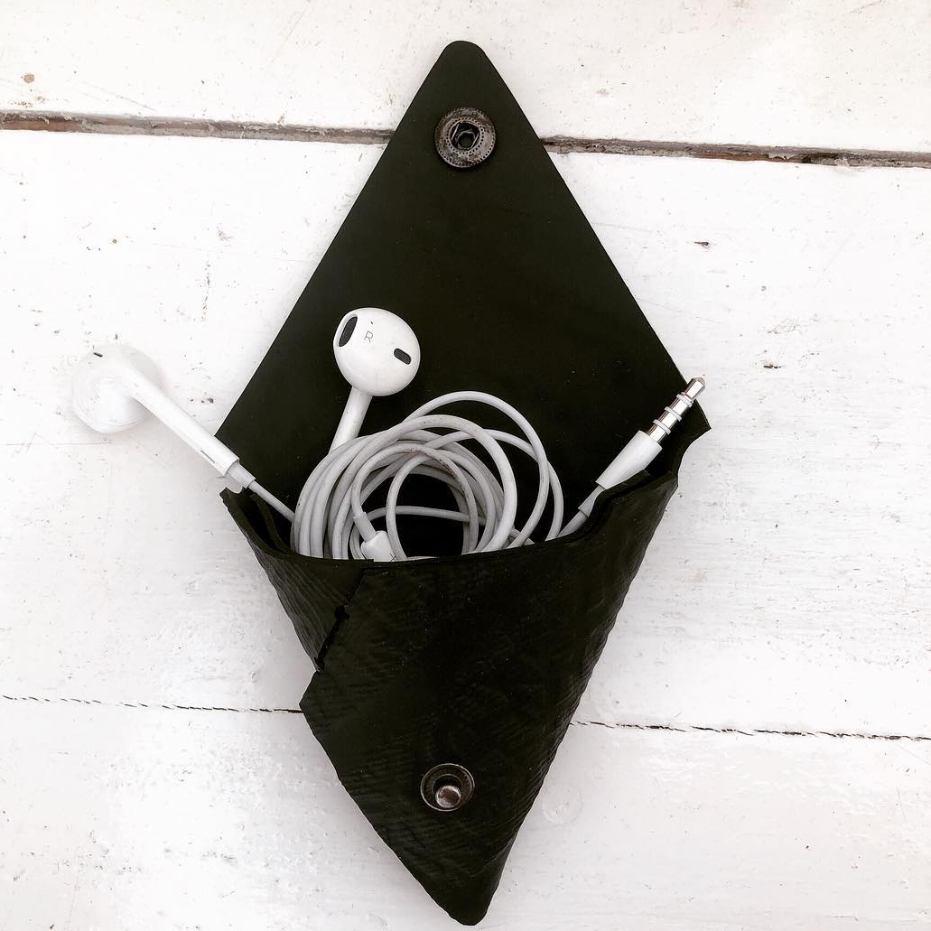 Paguro Upcycle recycled rubber coin pouch in black holding a pair of white earbuds