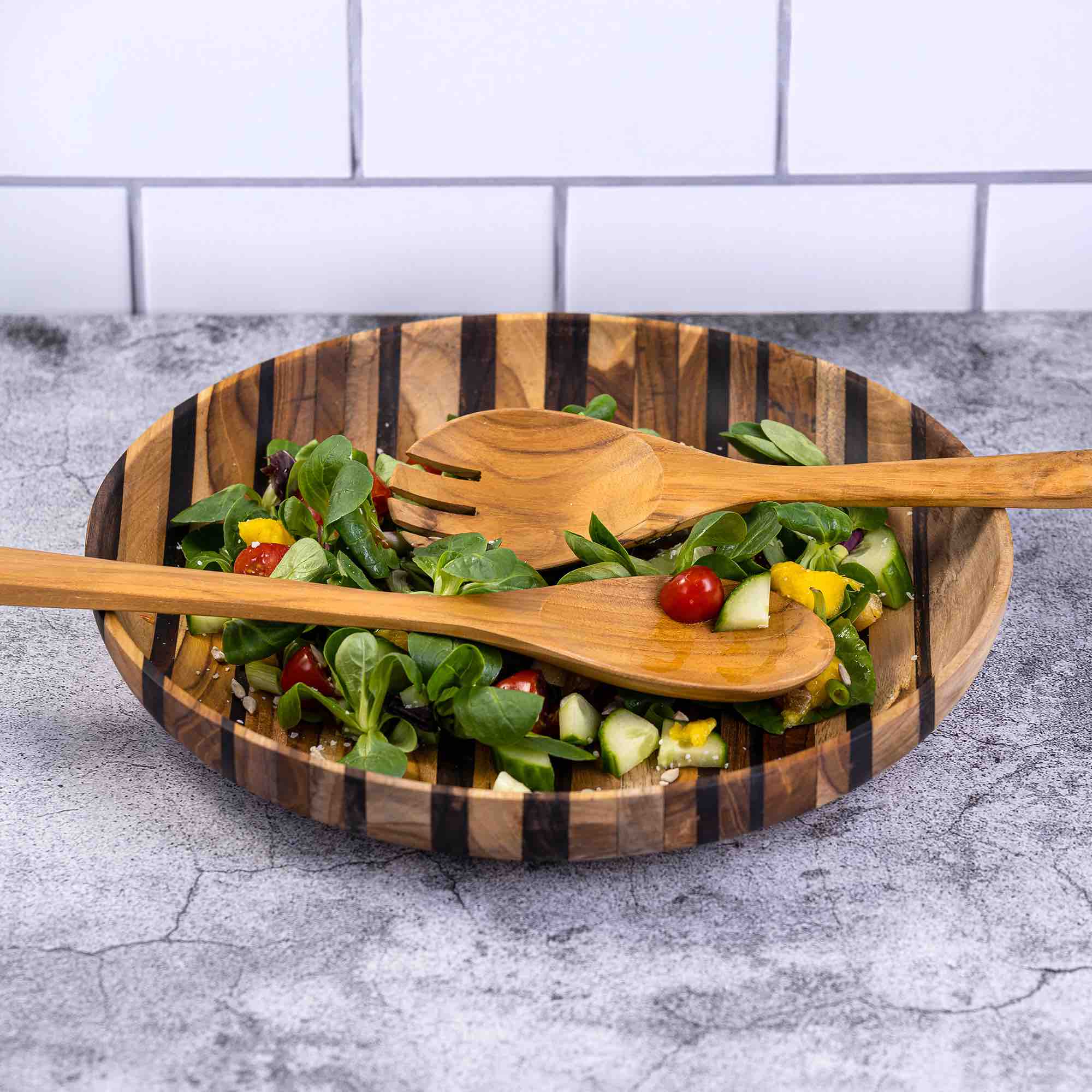 Upcycled wooden salad servers spoon and fork in striped wooden bowl with fresh vegetable salad