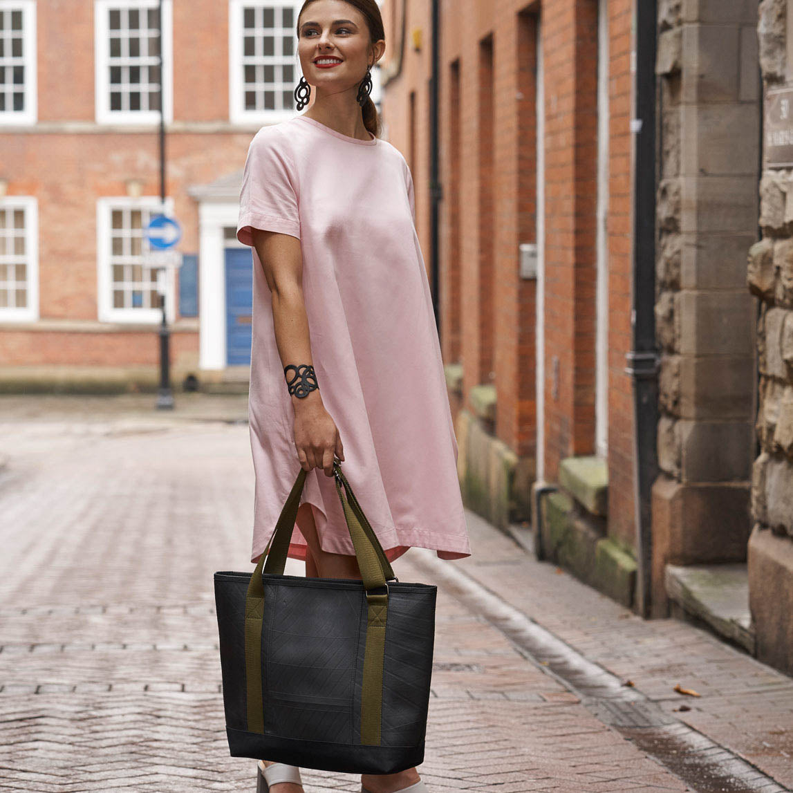 Woman carrying Paguro Upcycle vegan tote bag made from inner tube with green handles on city street