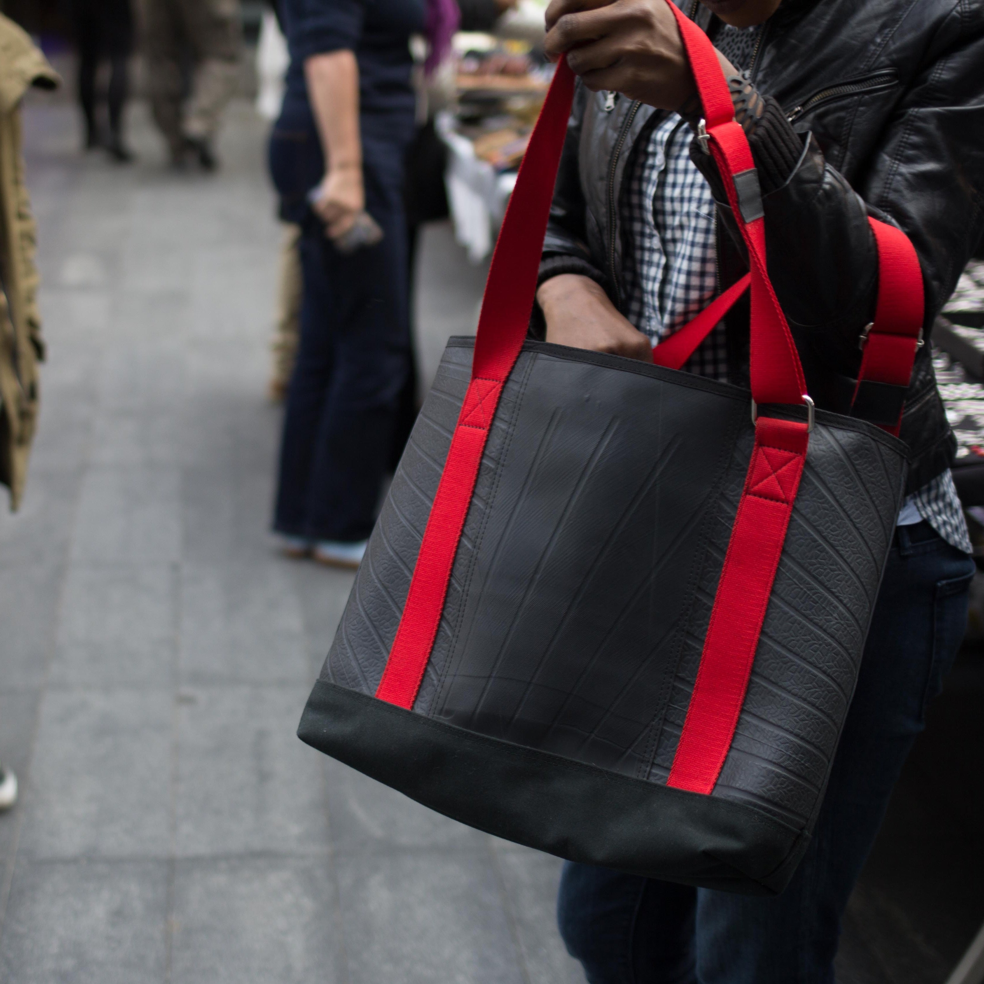 Paguro Upcycle vegan tote bag made from inner tube with red straps held by person outdoors