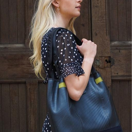 Paguro Upcycle recycled rubber tote bag in black carried by woman with blonde hair wearing black polka dot dress