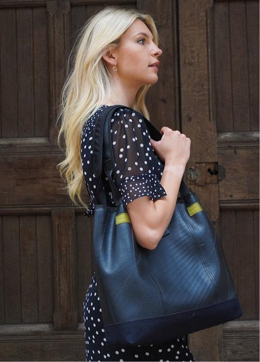 Paguro Upcycle recycled rubber tote bag in black carried by woman with blonde hair wearing black polka dot dress