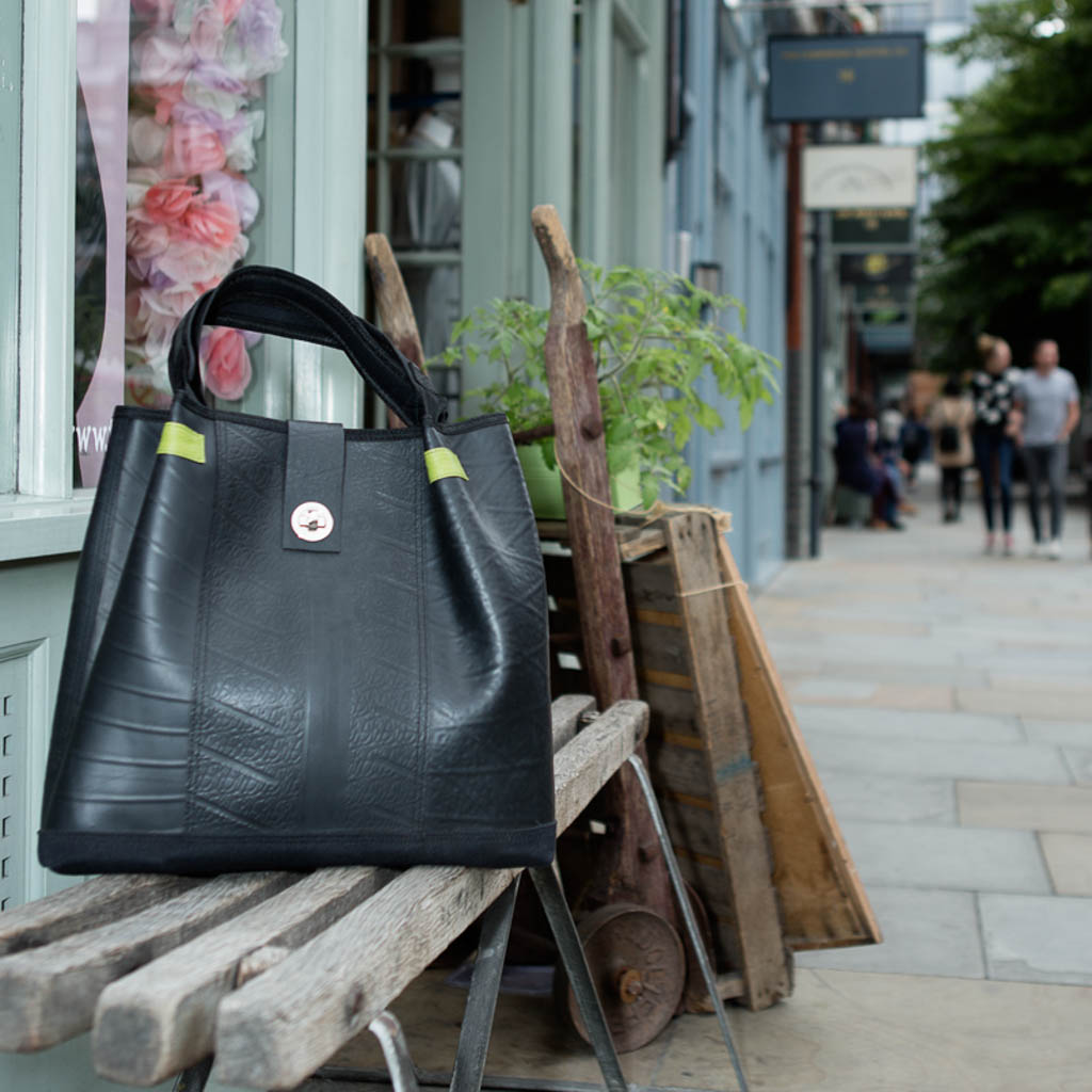 Paguro Upcycle recycled rubber tote bag in black displayed on outdoor wooden bench