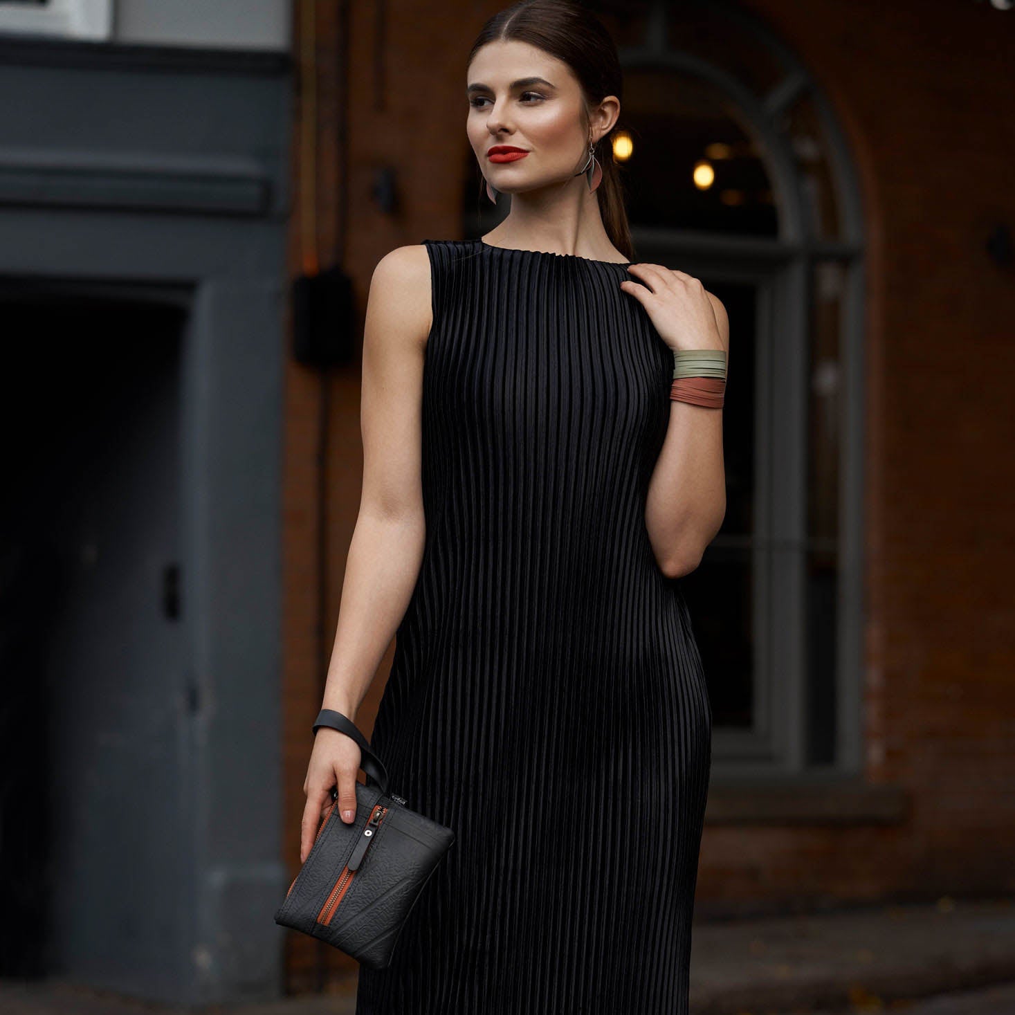 Woman in black dress holding Paguro Upcycle vegan wristlet pouch with wrist strap outdoors